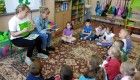 Zdjęcie przedstawia dzieci z grupy Motylków, które słuchają książki czytanej przez mamy.